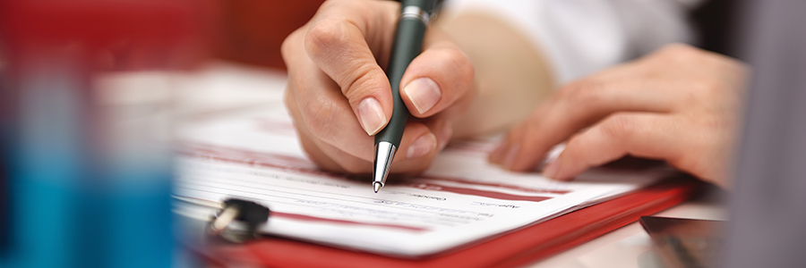Doctor filling medical history with pen on clipboard.